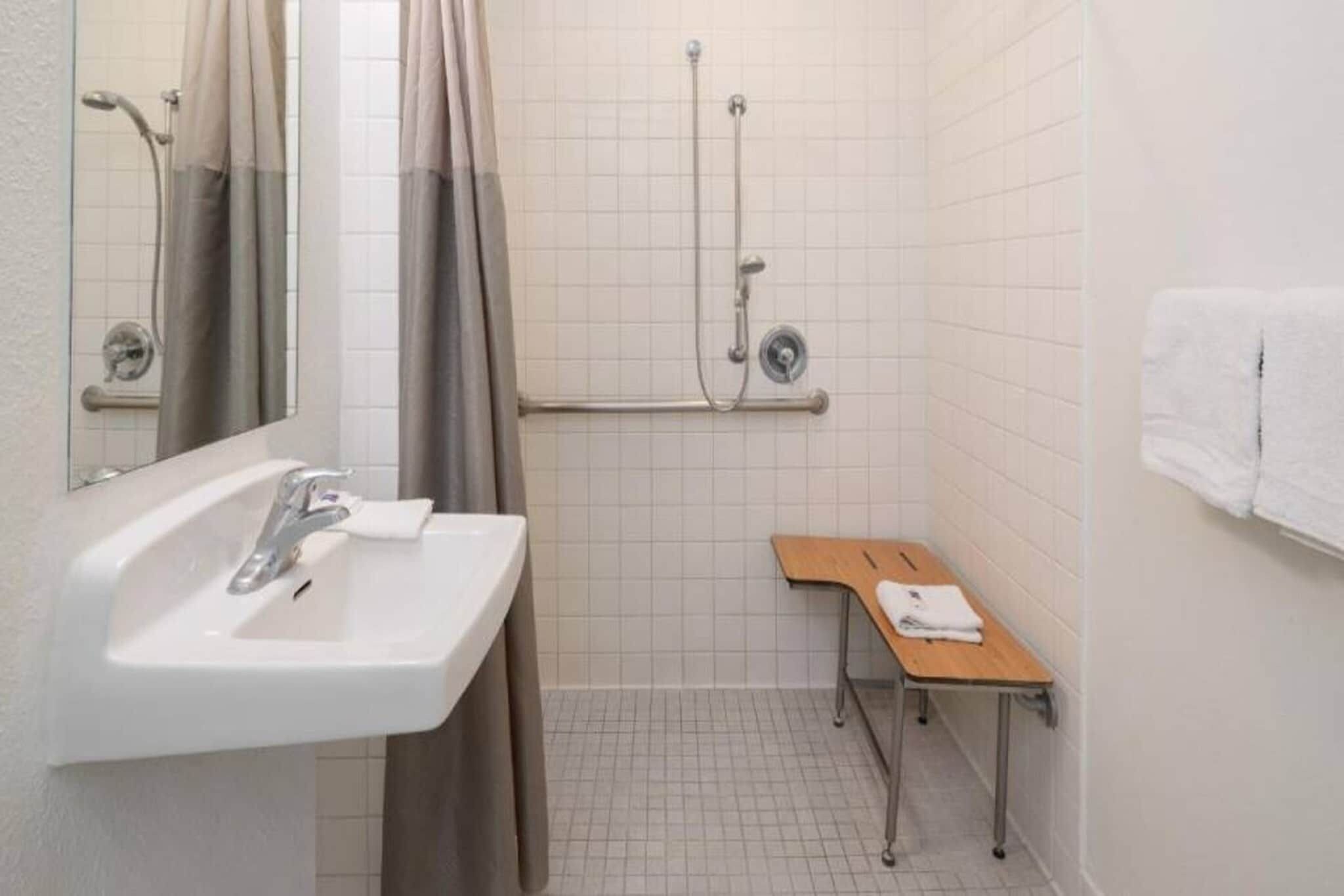 A bathroom with a sink, mirror, shower, and a small table.