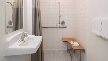 A bathroom with a sink, mirror, shower, and a small table.