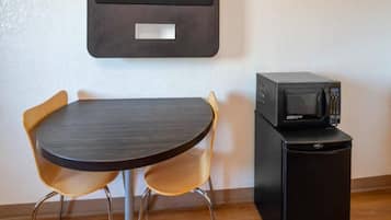 A compact room with a small round table and two chairs, a microwave on a cabinet, and a wall-mounted television.