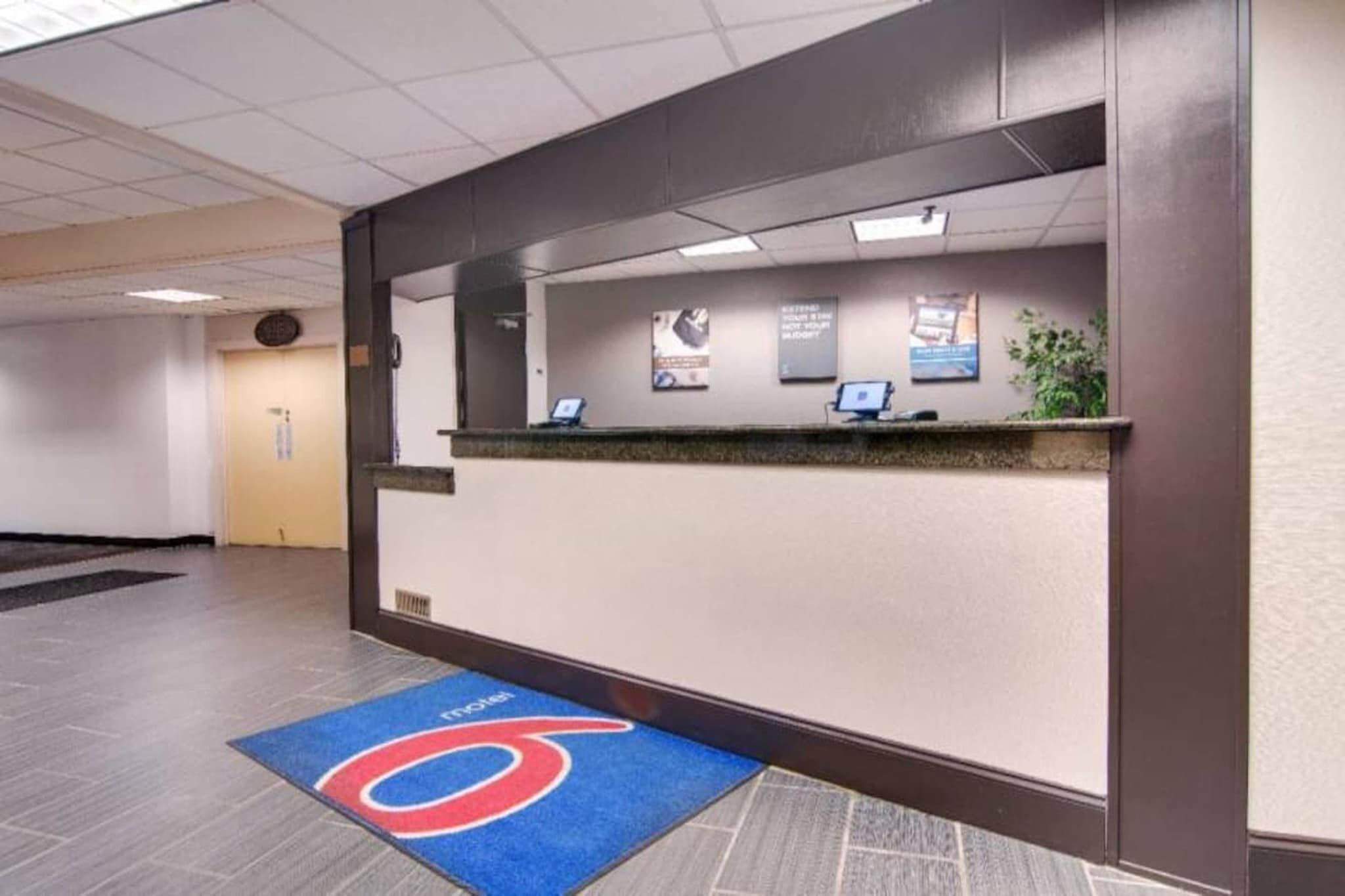 Zona de recepción con mostrador, alfombra azul con logotipo y un panel informativo en la pared.