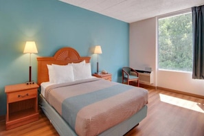 A hotel room with a bed, two bedside tables, a chair, a desk, and a window with curtains. - 1 Queen Bed | Non-Smoking (Clarion)