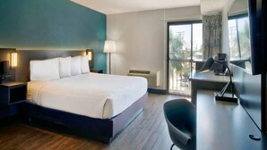 Habitación de hotel con cama, mesita de noche, lámpara, escritorio, silla y un ventanal grande.