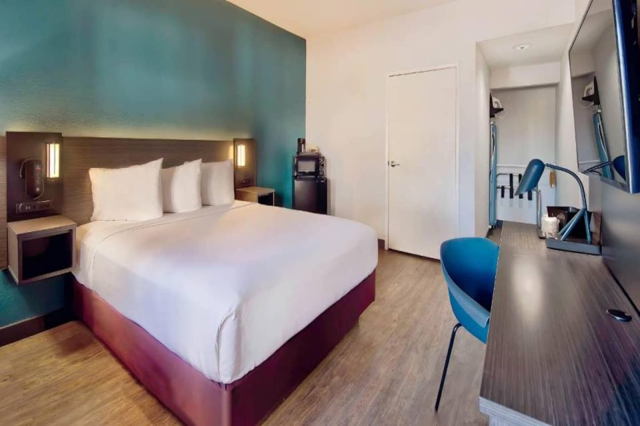 Una camera d'albergo con un letto, comodini, una scrivania con una sedia, uno specchio e una porta che dà su un'altra stanza.