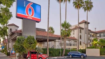 Un hôtel doté d’un grand panneau numérique affichant la mention « 6 suites » et d’un parking où sont stationnées plusieurs voitures.