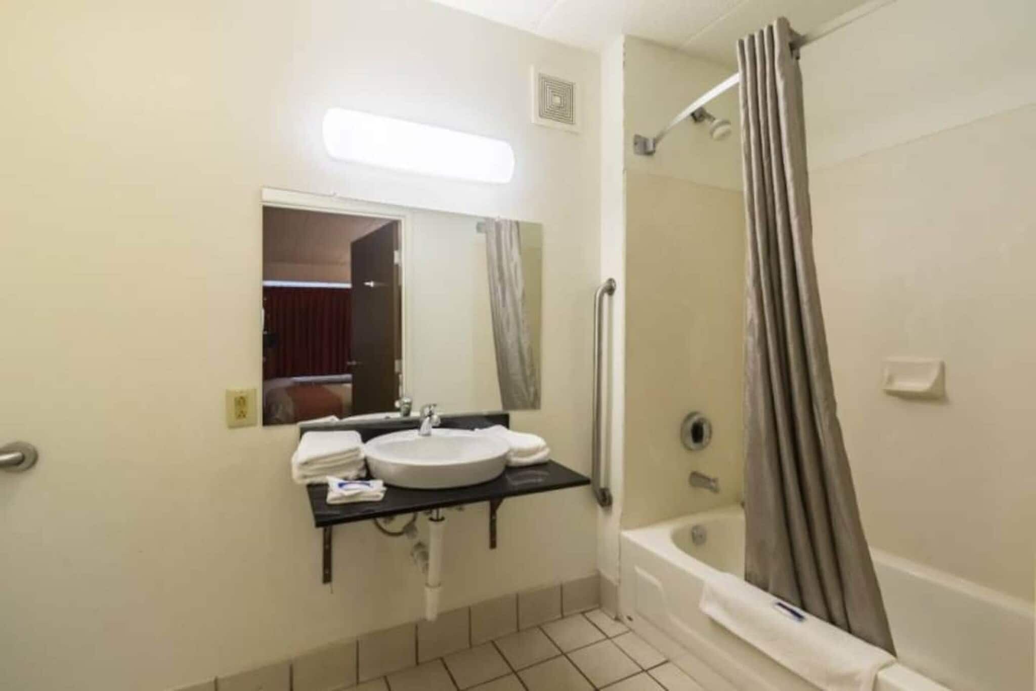 A bathroom with a shower, a sink, a mirror, and a towel rack.