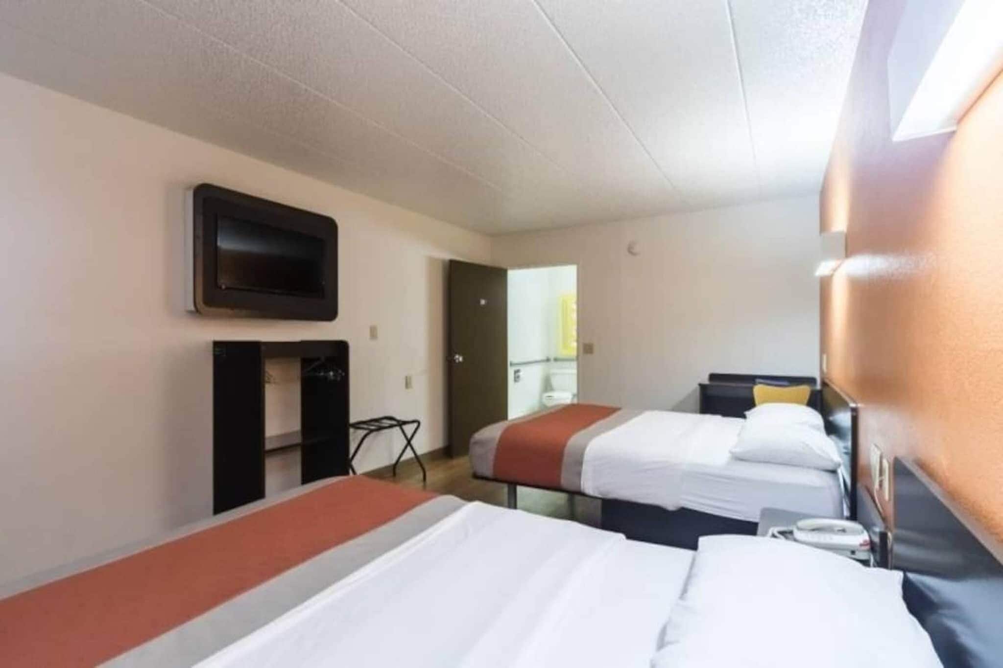 A hotel room with two beds, a television mounted on the wall, and a desk with a chair.