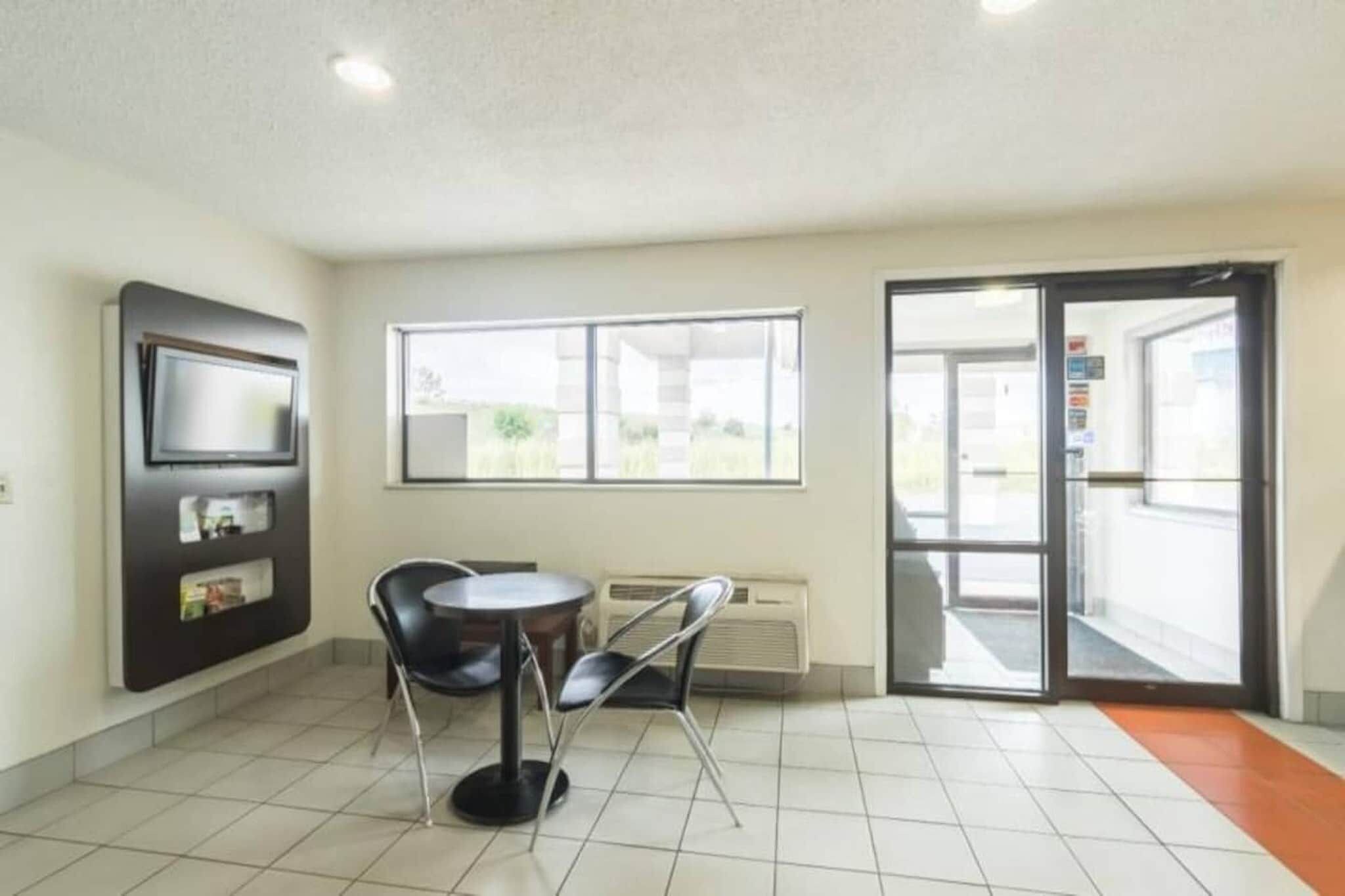 A room with a tiled floor, a table with chairs, a flat-screen TV mounted on the wall, and a large window with a view of the outdoors.