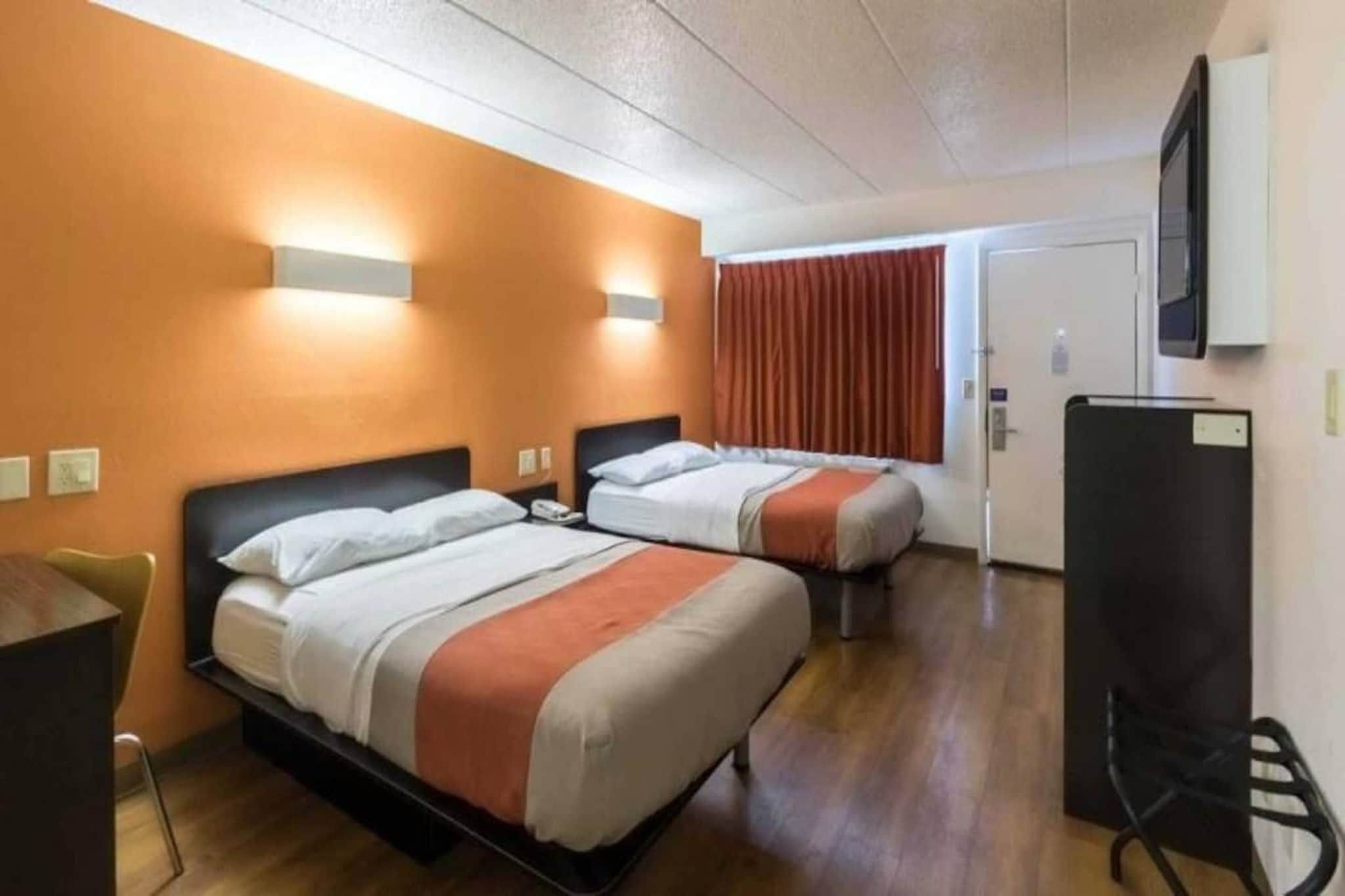 A hotel room with two beds, a desk, a chair, and a television.