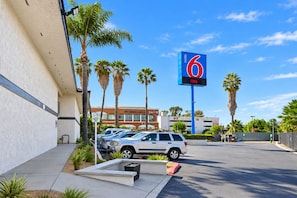 Ein Parkplatz mit einem Hinweisschild 'Motel 6', Palmen und einem Gebäude, an dem 'Desert Oasis' steht.