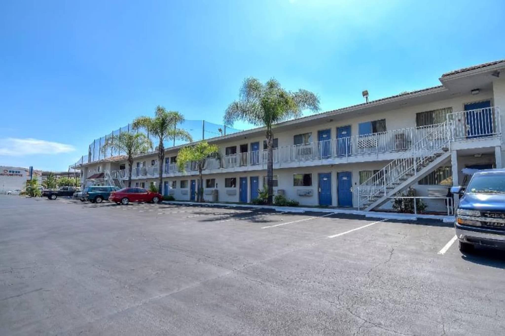 Motel amb un pàrquing, una cotxe vermell i un altre blau a la façana.