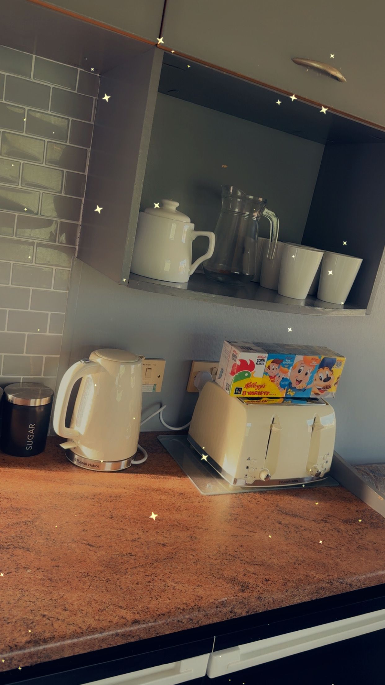 A kitchen with a coffee maker, a box of cereal, and a kettle on the counter.