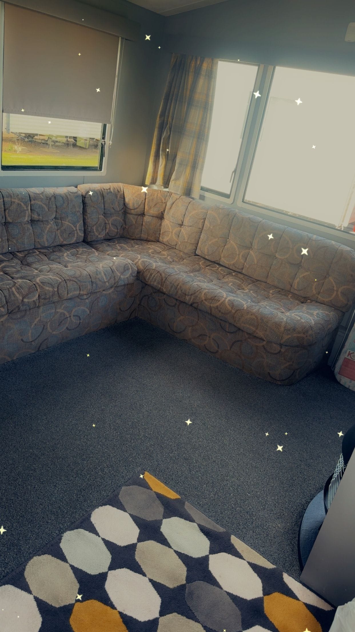 A sectional sofa with a patterned design, a patterned rug, and a window with curtains.