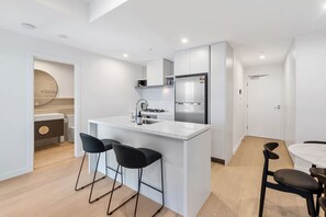 A modern kitchen with a central island, bar stools, and a dining area with a round table and chairs. - Modern 1BR Steps from Broadbeach Action (Broadbeach)