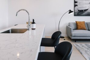 A modern kitchen with a marble countertop, a stainless steel sink, and a black chair. - Modern 1BR Steps from Broadbeach Action (Broadbeach)
