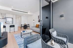 A modern apartment with a dining area, a living room with a sofa and chairs, a kitchen, and a balcony with wicker furniture. - Modern 1BR Steps from Broadbeach Action (Broadbeach)