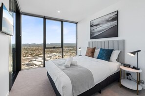A modern hotel room with a large bed, a city view, and a framed artwork on the wall. - Modern 1BR Steps from Broadbeach Action (Broadbeach)