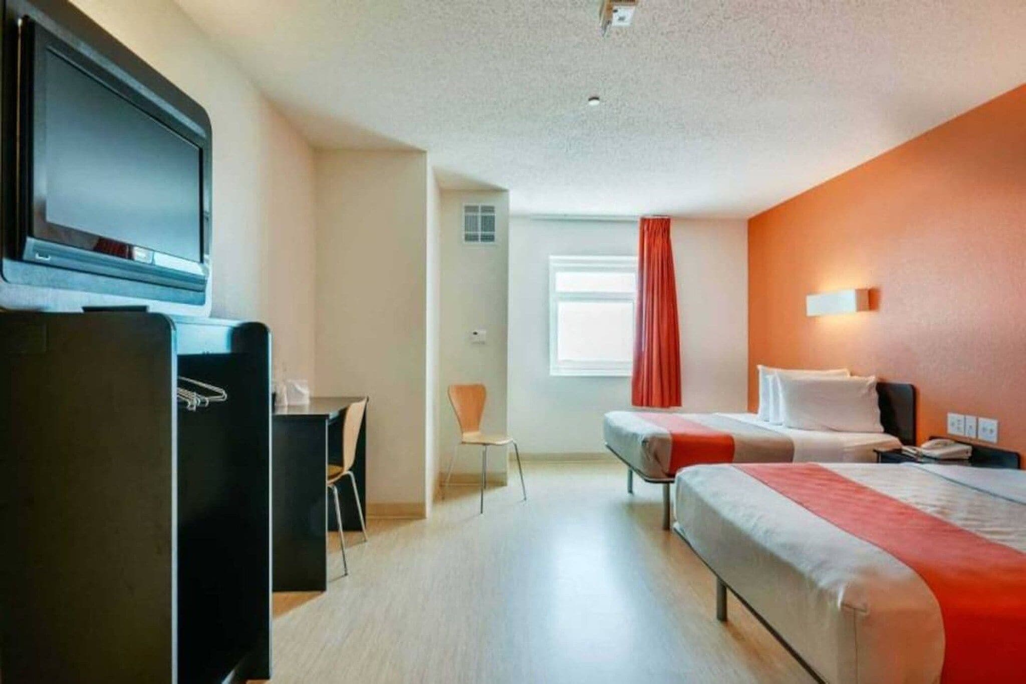 A hotel room with a bed, a desk, a chair, a television, and a window with curtains.