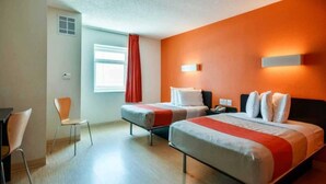 Una camera d'albergo con due letti, una scrivania, una sedia e una finestra con tende.
