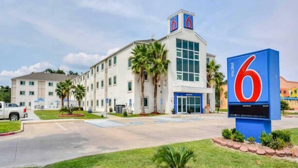 Un motel con un grande cartello con il numero '6', un parcheggio e un edificio con molte finestre e un tetto piatto.