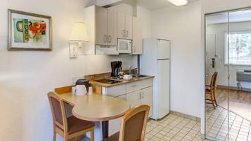 Uma cozinha compacta com mesa e cadeiras, micro-ondas, máquina de café e geladeira.