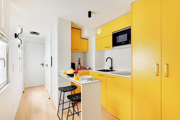 Une cuisine de taille réduite avec des meubles de couleur jaune, un four à micro-ondes de la marque Bosch et un tabouret de bar.