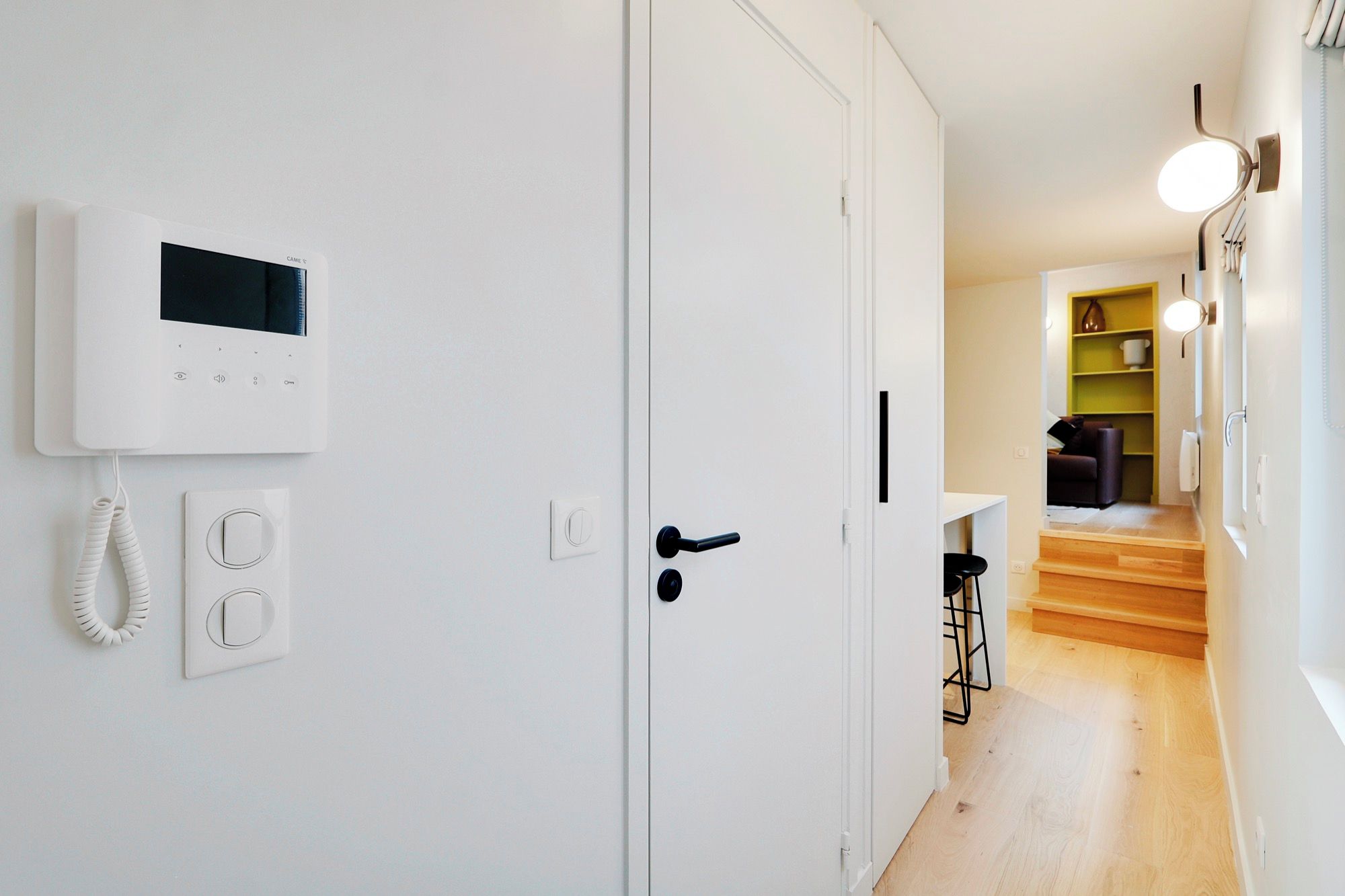Ein Flur mit einer weißen Tür, einem Thermostat und einem Telefon.