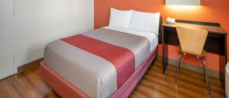 Una habitación de hotel con cama, escritorio, silla y lámpara de pared.