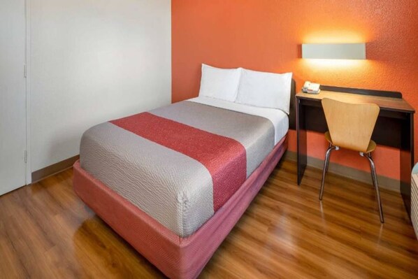 A hotel room with a bed, a desk, a chair, and a wall-mounted lamp.