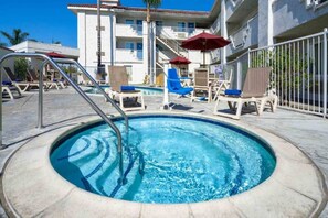 A swimming pool with lounge chairs and umbrellas, surrounded by a building with multiple balconies.