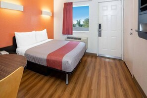 Een hotelkamer met een bed, een bureau, een stoel, een raam met gordijnen en een deur.