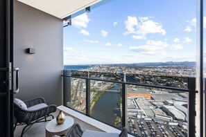 A balcony with wicker chairs and a small table, overlooking a cityscape with a river and airport. - Chic 1BR with Prime Broadbeach Location (Broadbeach)