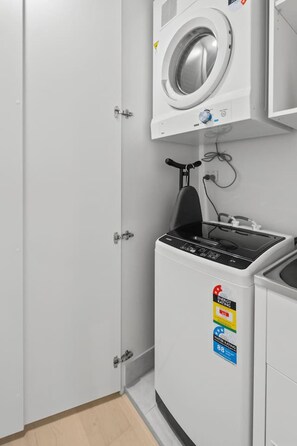 A laundry room with a front-loading washing machine and a dryer, a small ironing board, and a door with a handle. - Chic 1BR with Prime Broadbeach Location (Broadbeach)