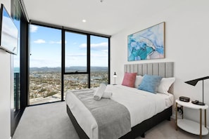 A modern bedroom with a large bed, a city view, and a painting on the wall. - Chic 1BR with Prime Broadbeach Location (Broadbeach)