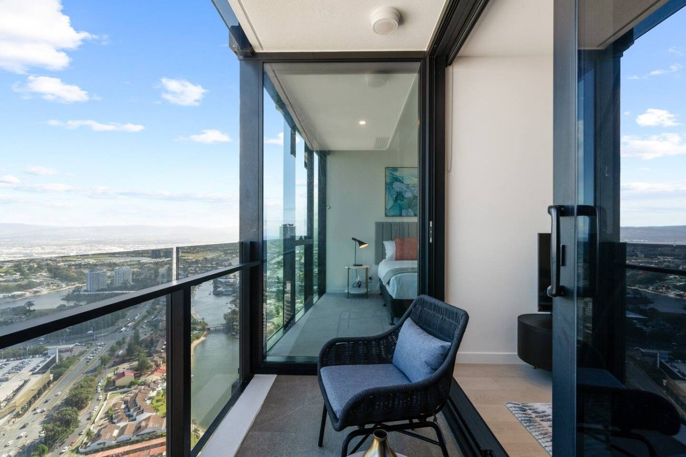 Un balcón moderno con vistas a la ciudad, una silla cómoda y un dormitorio minimalista con cama y un cuadro.
