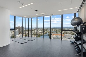 A spacious room with large windows offering a city view, a wall-mounted exercise equipment, and a yoga mat on the floor. - Chic 1BR with Prime Broadbeach Location (Broadbeach)