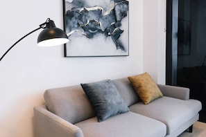 A grey sofa with two cushions, a black floor lamp, and a framed abstract painting on the wall. - Chic 1BR with Prime Broadbeach Location (Broadbeach)