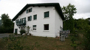 A two-story building with a balcony, a small garden, and a wooden fence.