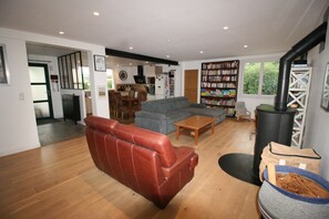 Ein Wohnzimmer mit einem roten Ledersofa, einem grauen Couch und einem Couchtisch aus Holz, außerdem ein Bücherregal voller Bücher.