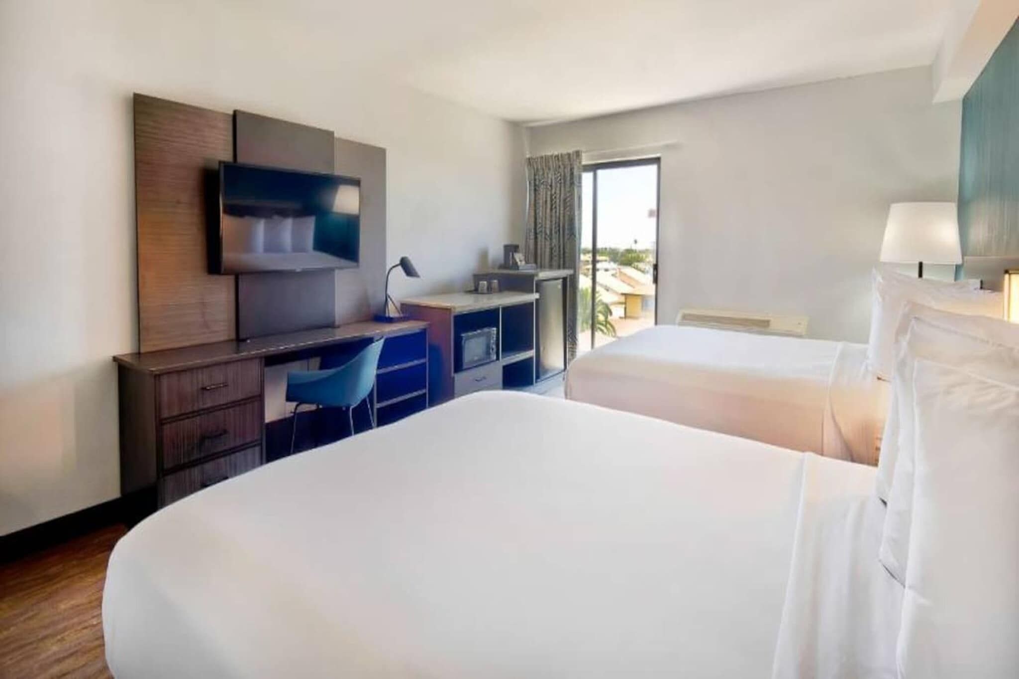 A hotel room with two beds, a desk, a television, and a window with curtains.