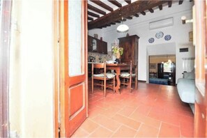 A room with a tiled floor, a wooden dining table with chairs, a kitchen area with cabinets, and a ceiling with exposed beams. - Rosi's Terrazzino – Relaxation and an Authentic Atmosphere in the Village (Castiglione della Pescaia)