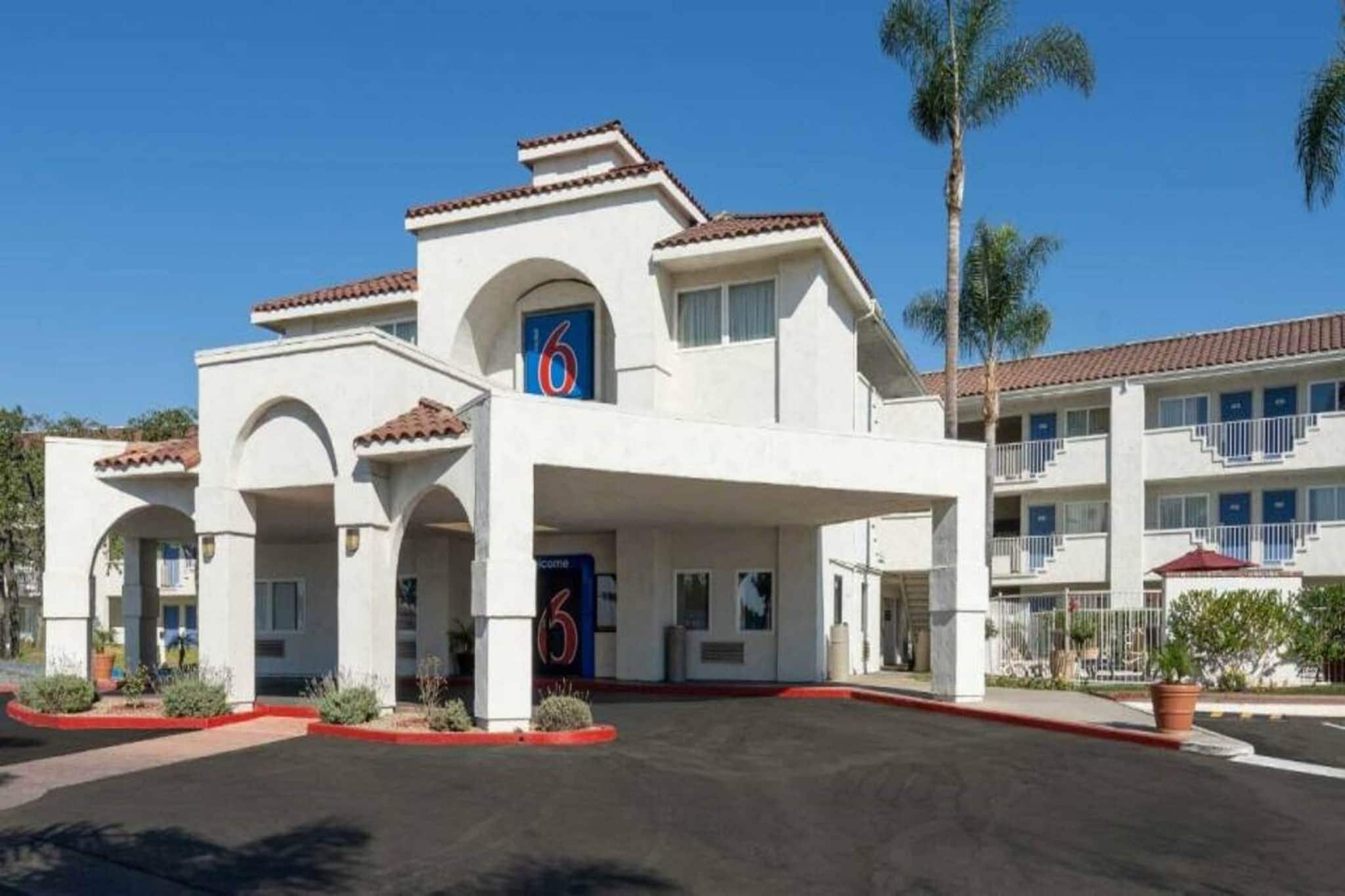 A multi-story hotel with a central entrance, multiple balconies, and a parking lot.