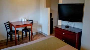 Een hotelkamer met een houten tafel, twee stoelen, een televisie op een dressoir en een rode kast.