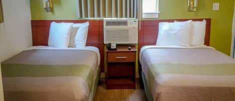 Una habitación de hotel con dos camas, una mesita de noche con lámpara, unidad de aire acondicionado y ventana con cortinas.