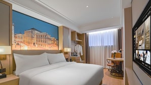 Una habitación de hotel con una cama grande, un escritorio, una silla, una mesa con un jarrón de flores y un ventanal con cortinas.