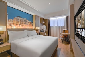 A hotel room with a large bed, a desk, a chair, a table with a vase of flowers, and a large window with curtains. - Vienna International Hotel  (shenzhen)