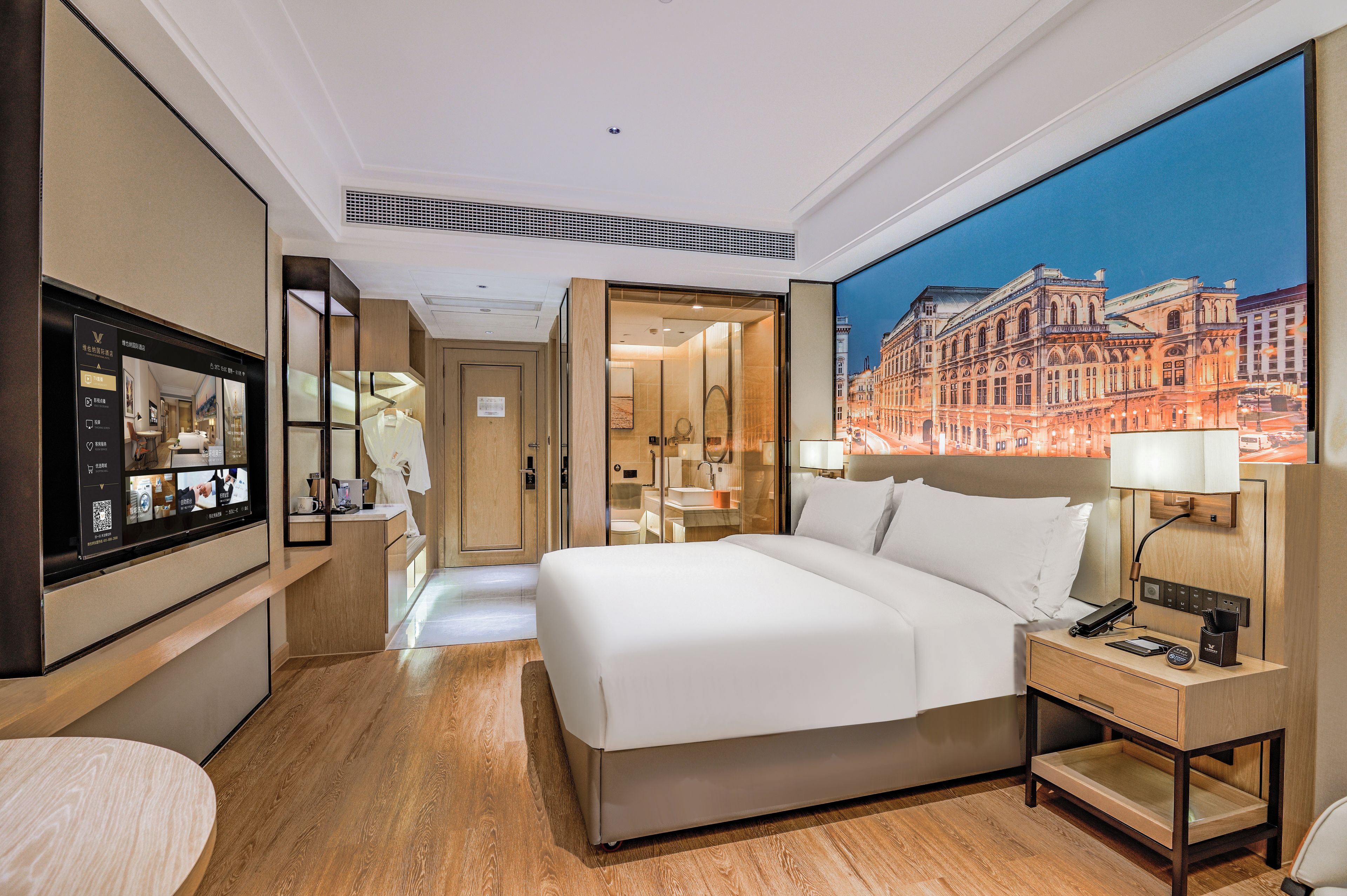 Une chambre d’hôtel avec un grand lit, un bureau avec une lampe, une télévision et une vue sur le paysage urbain.