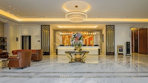 Un vestíbulo de hotel con piso de mármol, asientos de cuero, un mostrador de recepción y una araña.