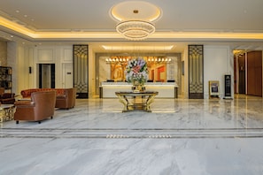 A hotel lobby with a marble floor, leather seating, a reception desk, and a chandelier. - Vienna International Hotel  (shenzhen)