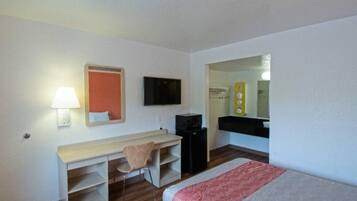 A hotel room with a bed, a desk, a chair, a television, a mirror, and a small black cabinet.