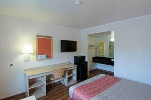 Ein Hotelzimmer mit einem Bett, einem Schreibtisch, einem Sessel, einem Fernseher, einem Spiegel und einem kleinen schwarzen Schrank.